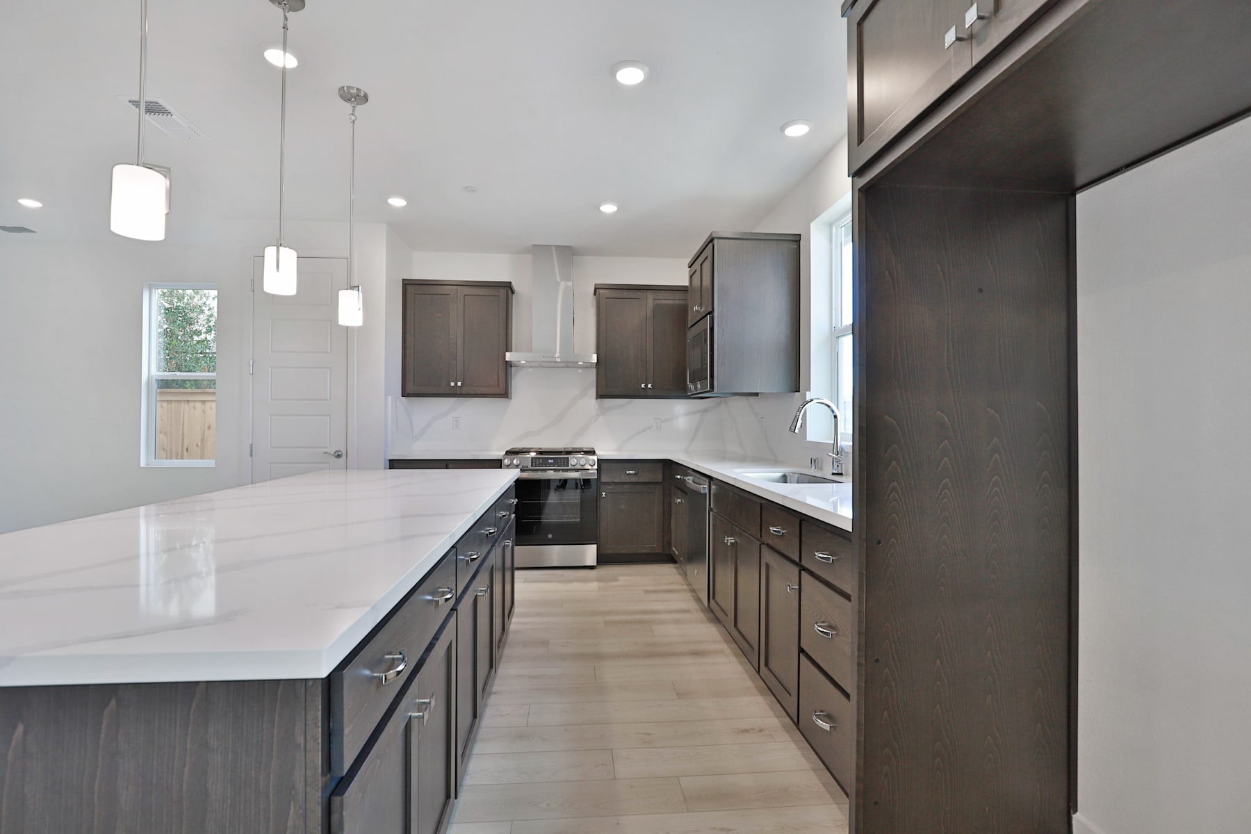 A modern, well-lit kitchen with dark wood cabinets, white countertops, and pendant lighting fixtures.
