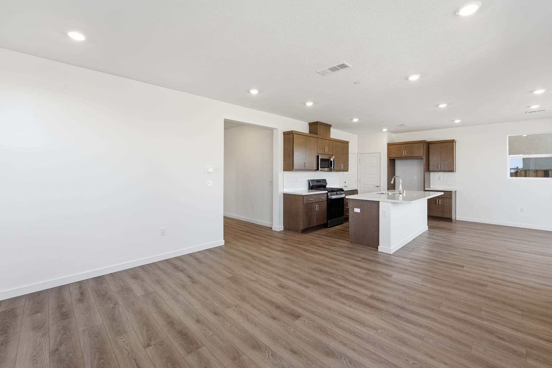 A modern, open-concept kitchen and living space with white walls, wood-look flooring, and dark wood cabinetry.