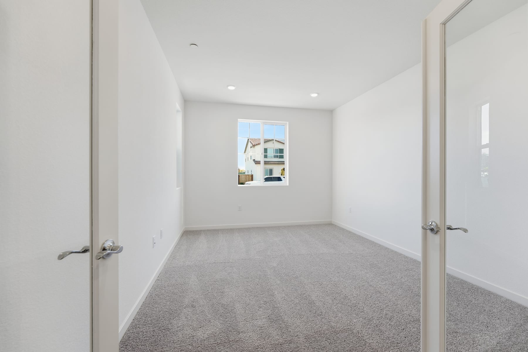 A bright, empty hallway with white walls, gray carpeting, and two closed doors visible in the background.