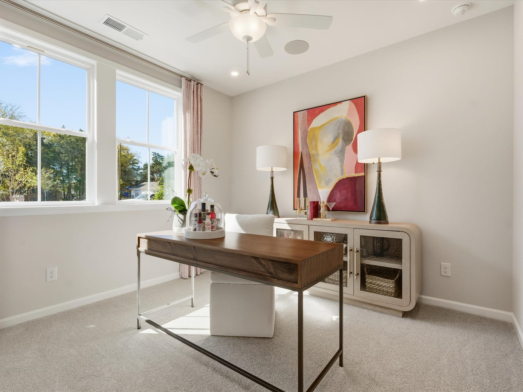 A modern and stylish home office space with a wooden desk, abstract artwork, and large windows providing natural light.