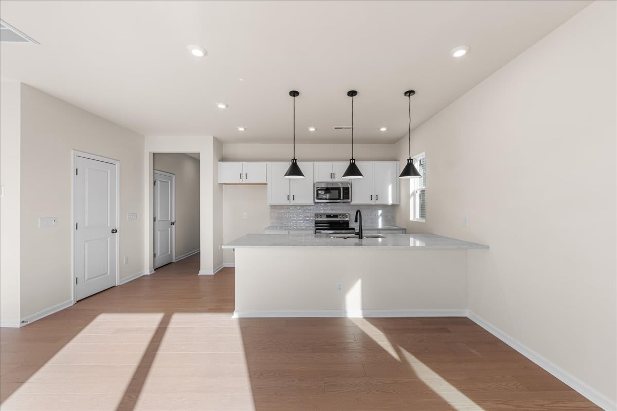 A modern, open-concept kitchen with white cabinets, a marble countertop, and pendant lighting fixtures, set against a hardwood floor and a bright, airy space.