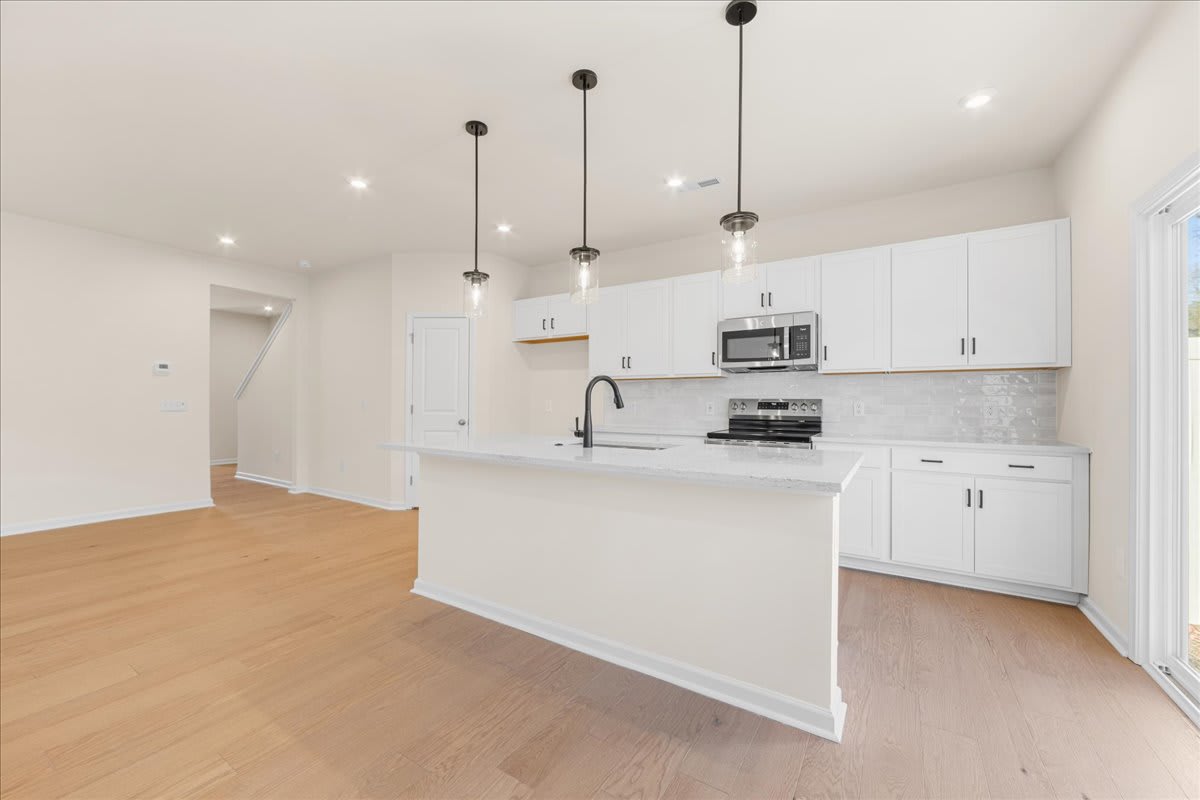 A modern, open-concept kitchen with white cabinets, a sleek countertop, and pendant lighting fixtures, set against a backdrop of hardwood floors and a bright, airy space.