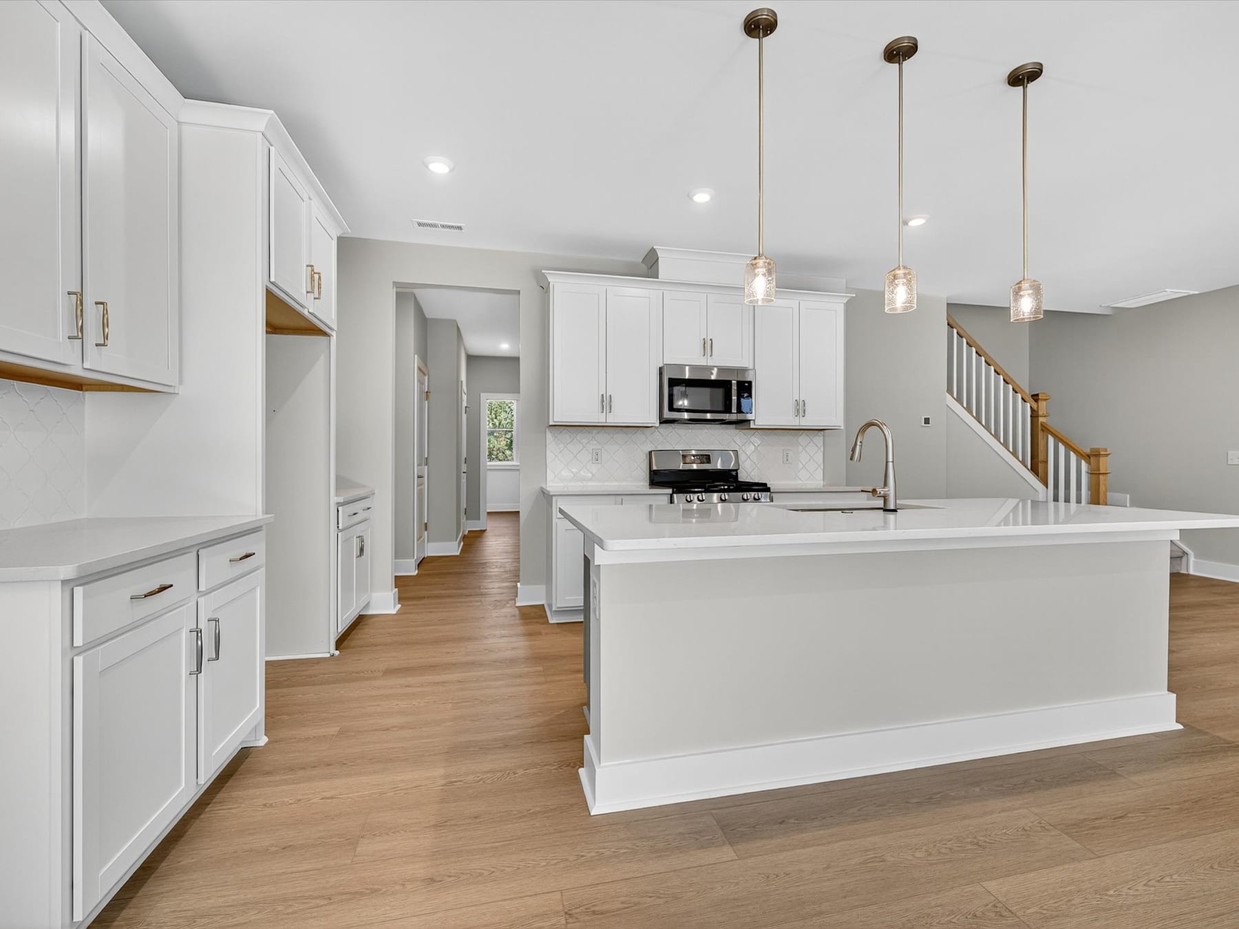 A modern, open-concept kitchen with white cabinets, a central island, and pendant lighting fixtures, set against a hardwood floor.