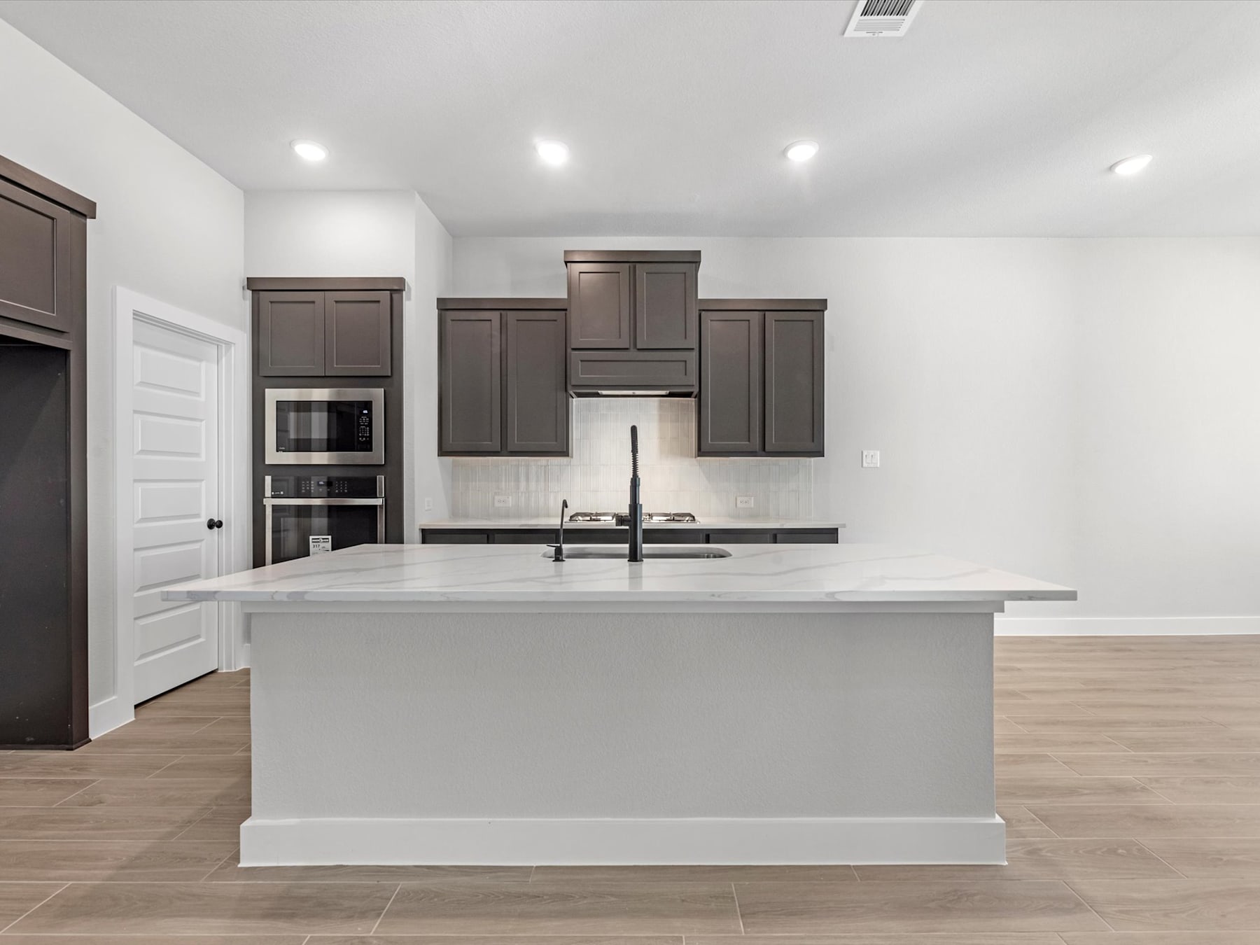 A modern kitchen with dark cabinets, a white countertop, and a central island in a spacious, well-lit room with hardwood floors.