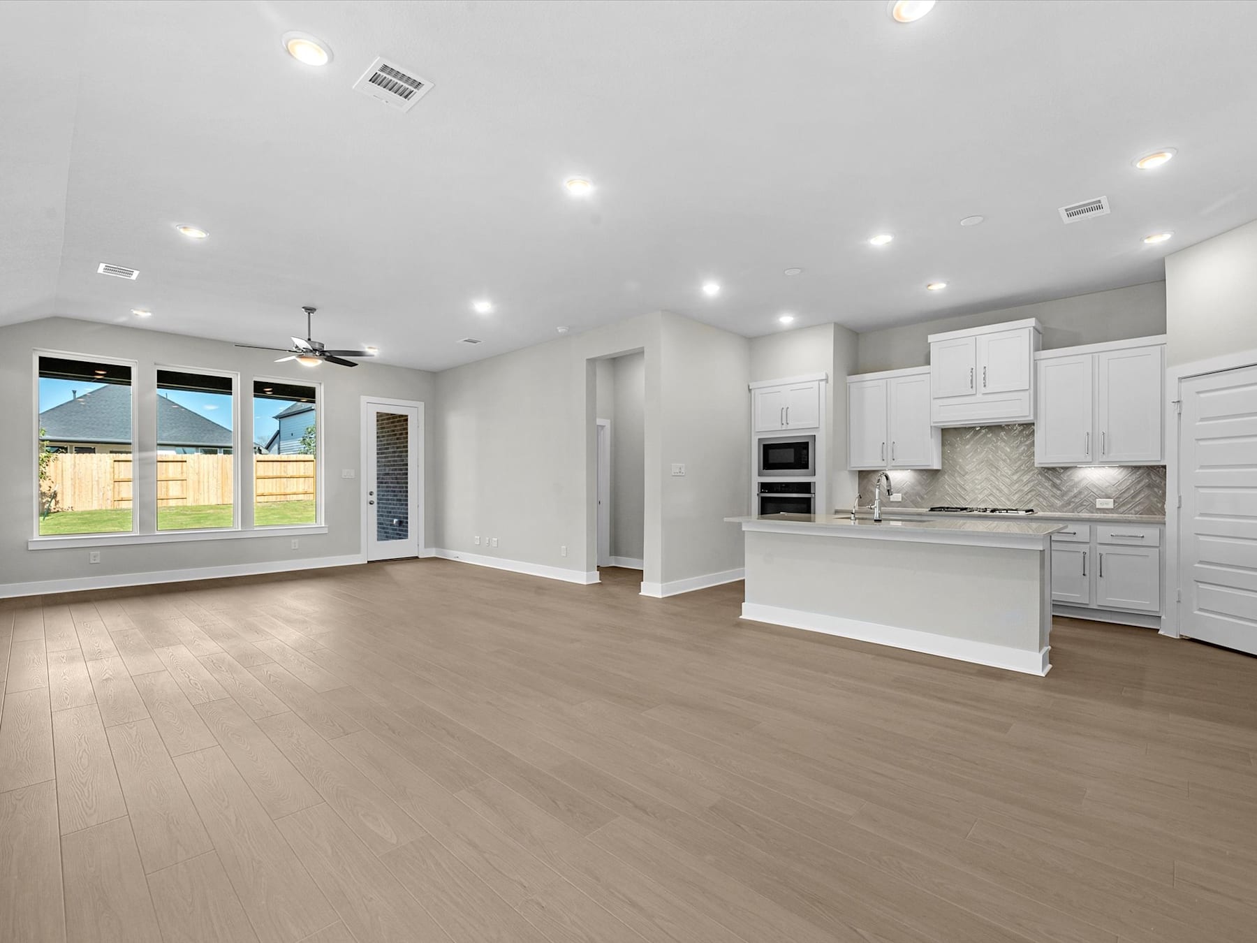 A spacious, open-concept living area with a modern kitchen, hardwood floors, and large windows allowing natural light to fill the space.
