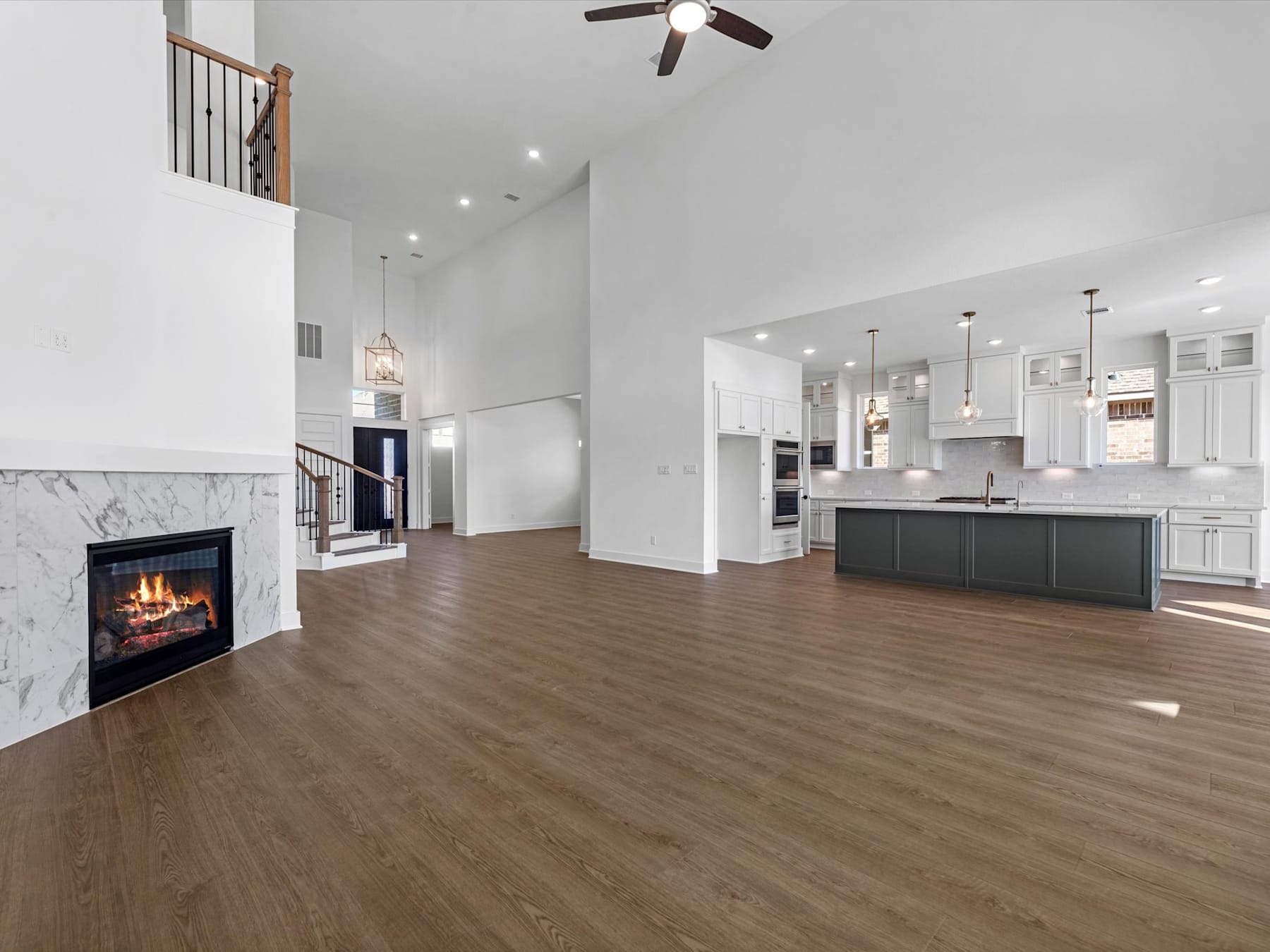 A spacious and modern open-concept living area with a fireplace, hardwood floors, and a kitchen visible in the background.