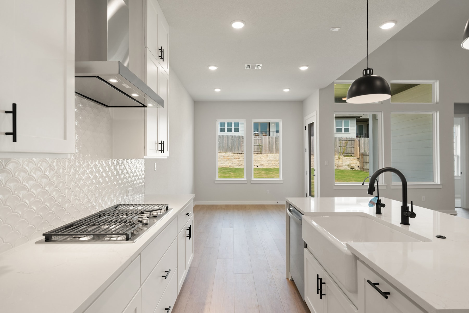 A modern, bright, and spacious kitchen with white cabinets, a gas stove, and a view of the backyard through large windows.