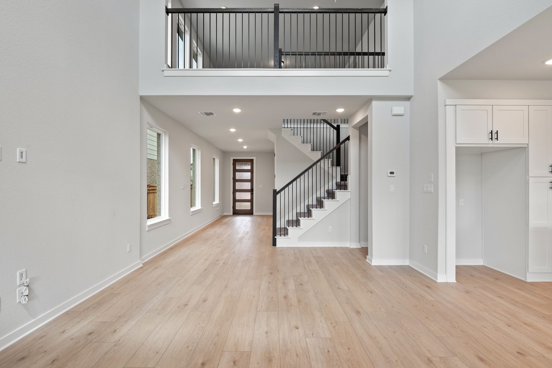 A spacious and modern interior with a wooden floor, white walls, and a staircase leading to an upper level.