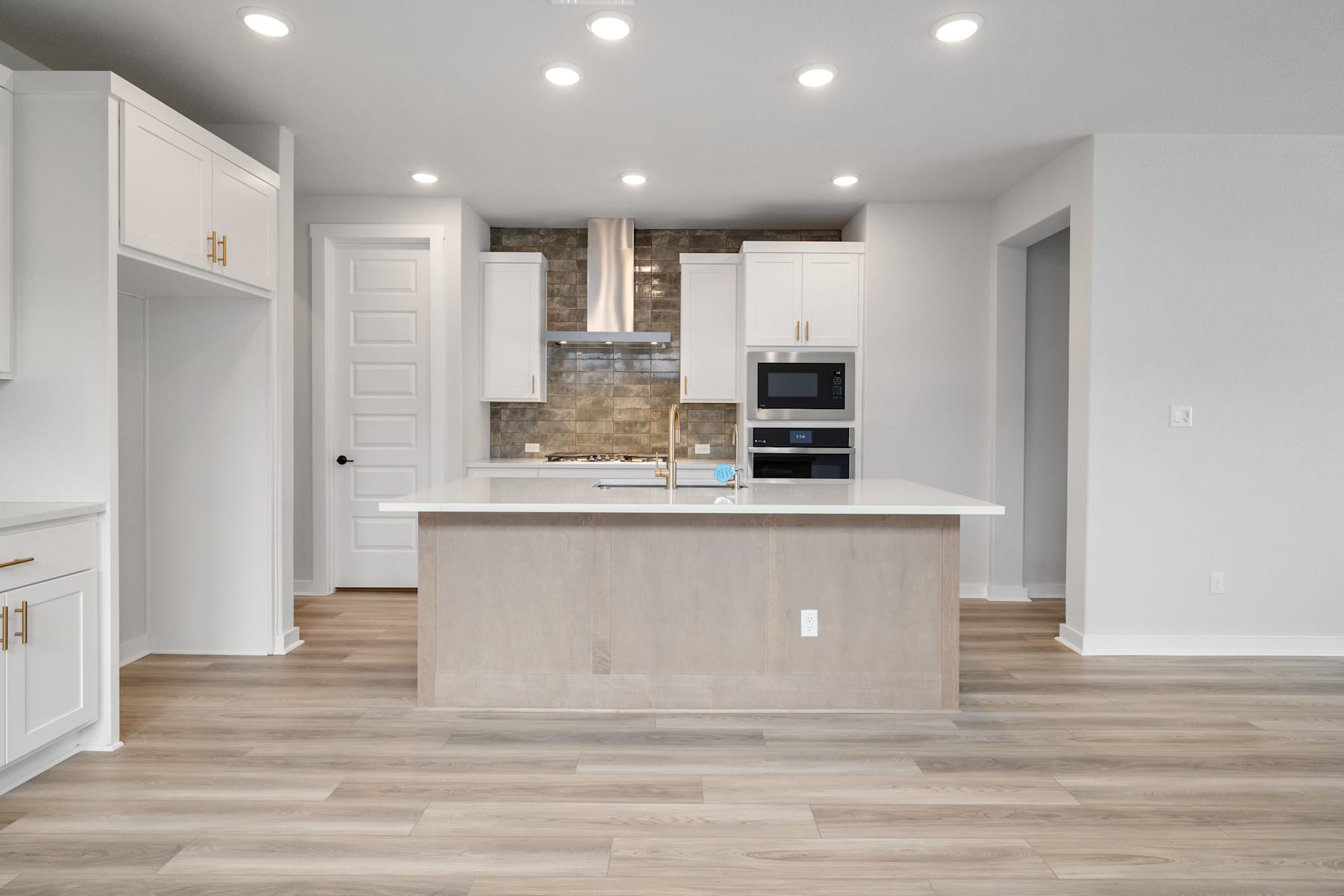 A modern, open-concept kitchen with white cabinets, a central island, and hardwood flooring, featuring recessed lighting and a brick accent wall.
