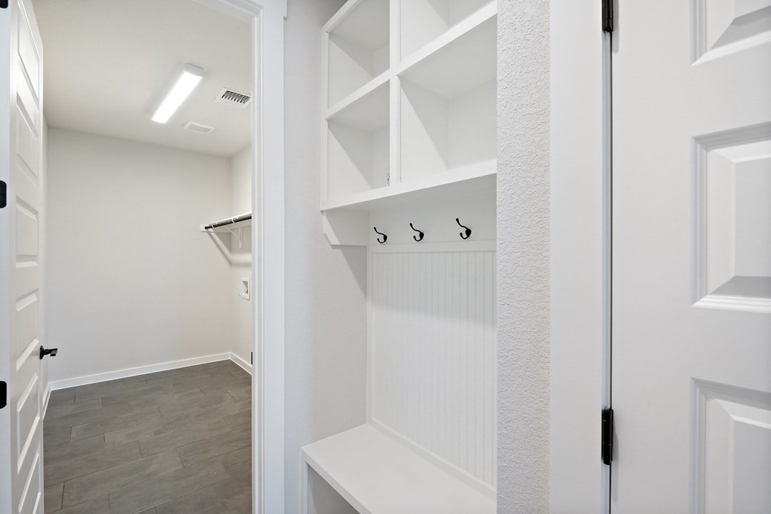 A bright, minimalist entryway with white walls, built-in shelving, and a tiled floor leading to an open doorway.