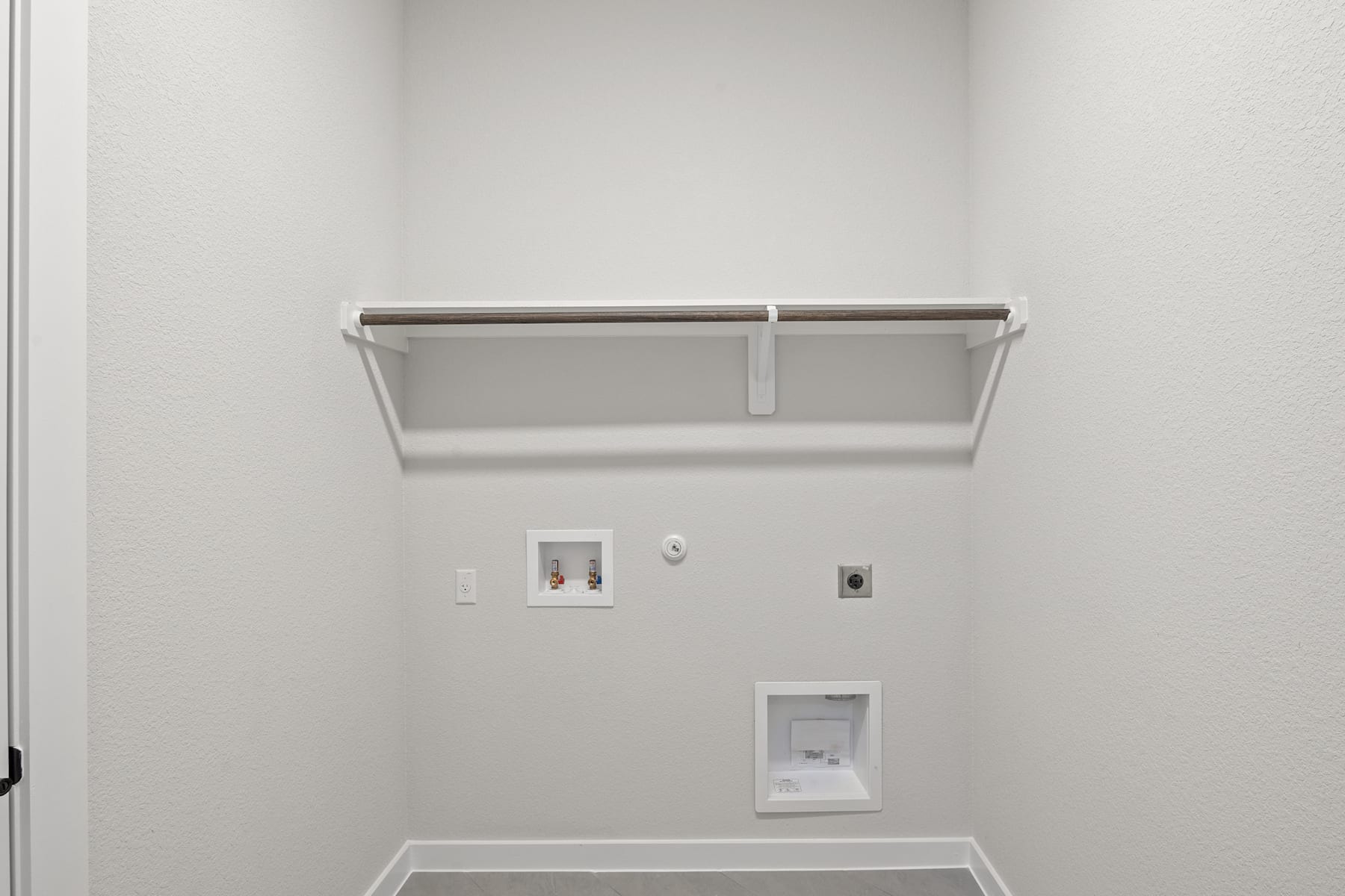 A simple, minimalist room with a white wall, a metal shelf, and electrical outlets on the wall.
