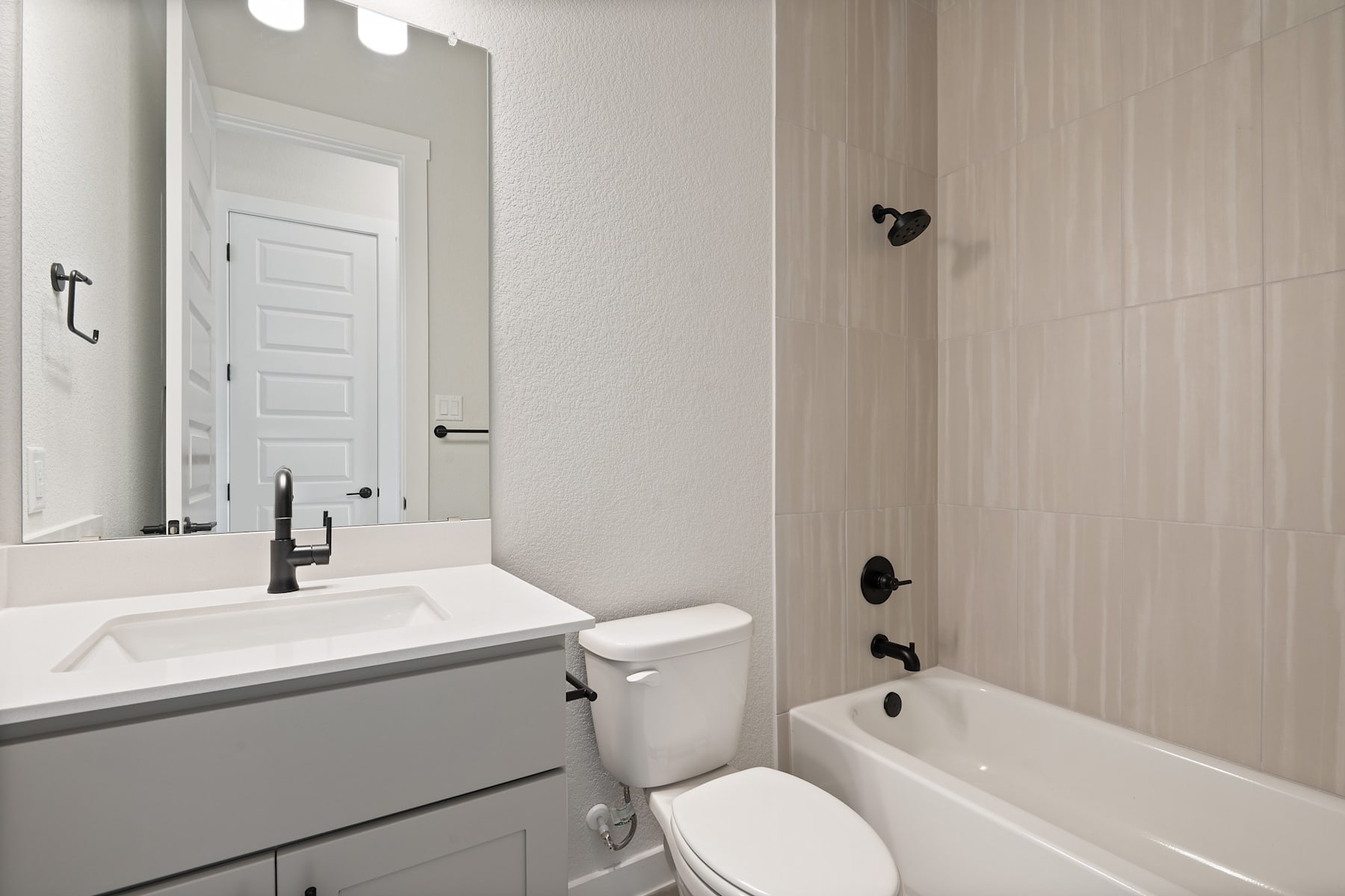 A modern, minimalist bathroom with a white vanity, a toilet, and a bathtub, all set against a neutral-toned wall and door.