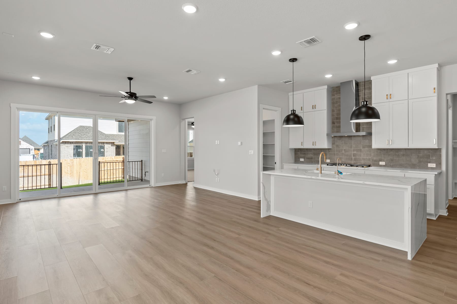 A modern, open-concept kitchen and living room with white cabinets, hardwood floors, and large windows providing natural light.