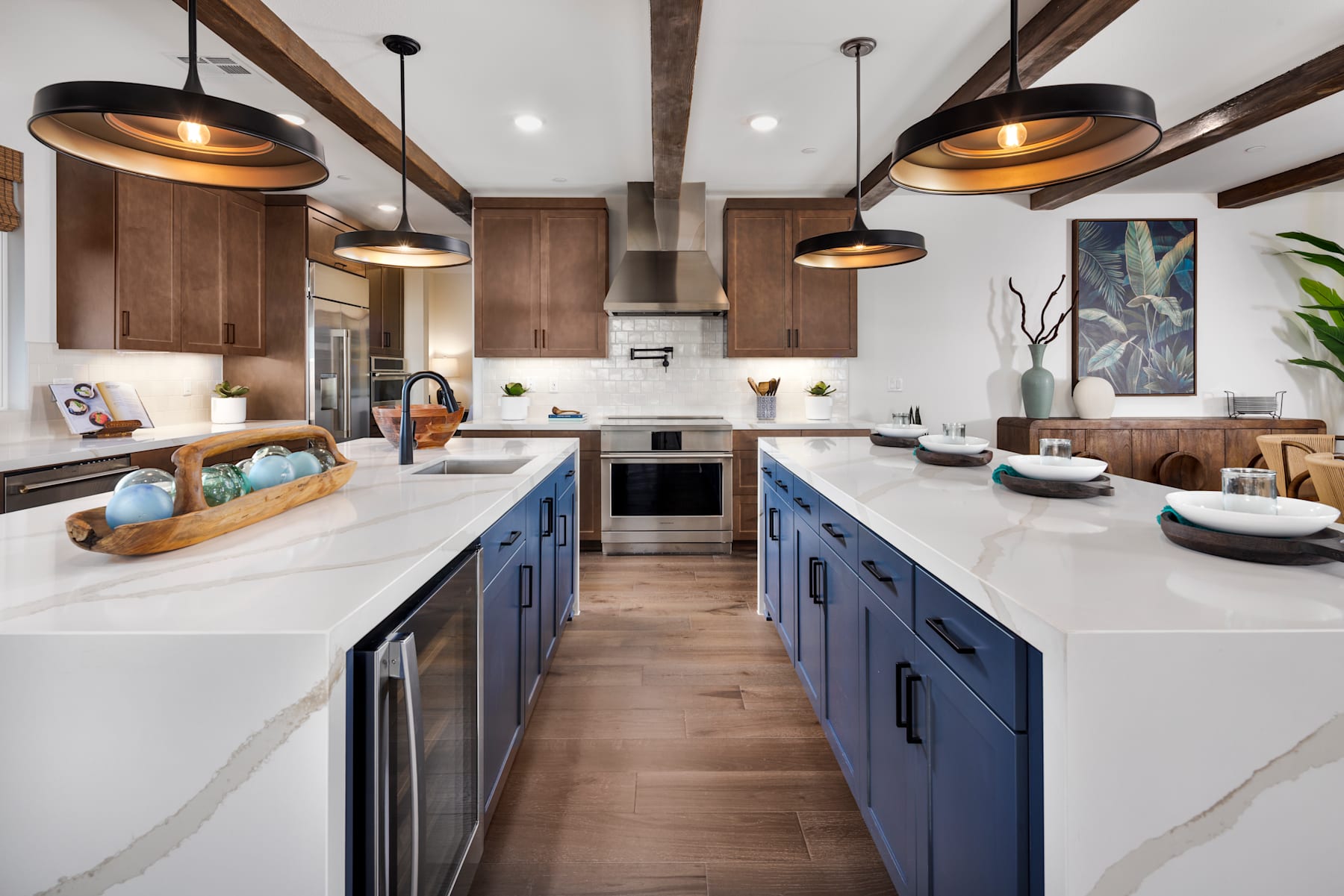 A modern and stylish kitchen with wooden beams, blue cabinets, and pendant lights, featuring a central island and various kitchen appliances and decor.