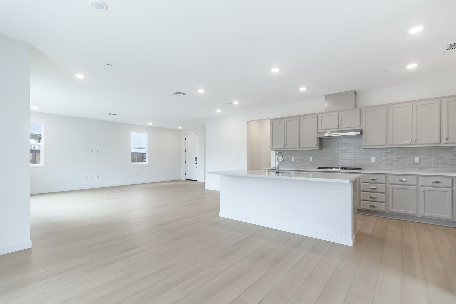 A spacious, open-concept kitchen and living area with light-colored cabinets, hardwood floors, and recessed lighting.