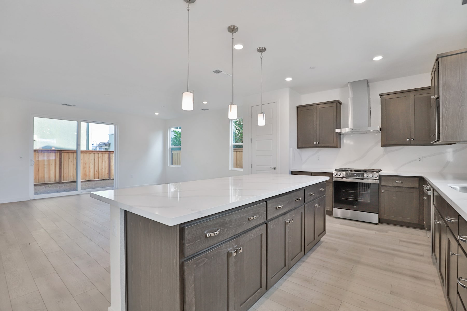 A modern, open-concept kitchen with dark wood cabinets, a large central island, and pendant lighting fixtures hanging from the ceiling.