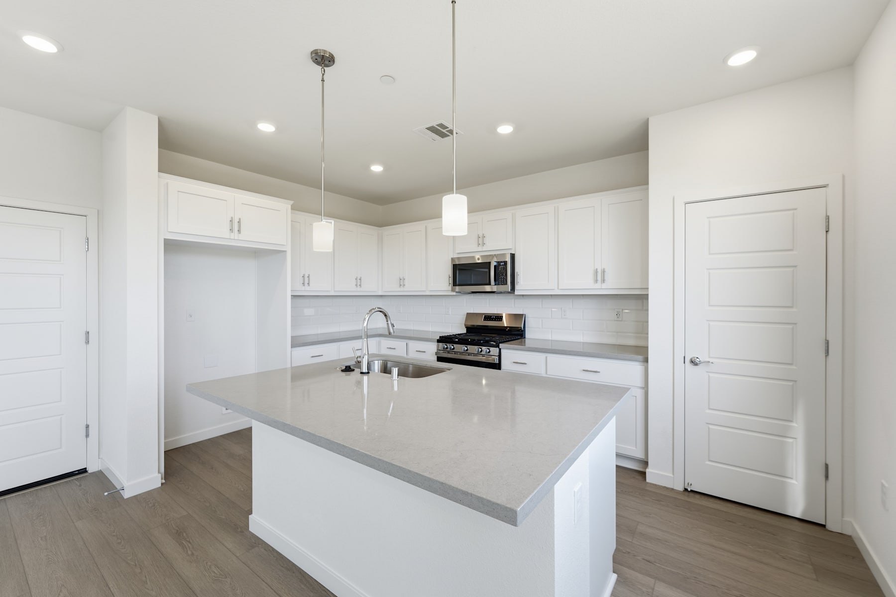 A modern, bright, and spacious kitchen with white cabinets, a gray countertop, and hardwood floors.