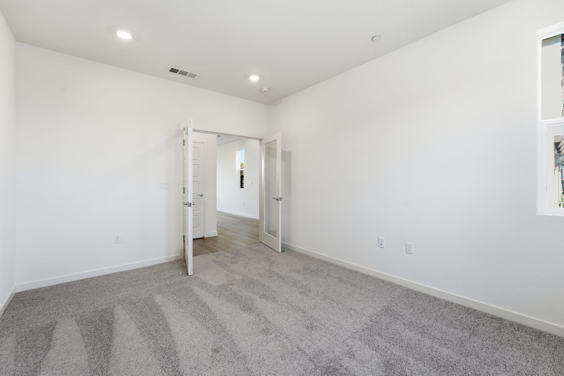 A spacious, minimalist room with white walls, gray carpeting, and two open doorways leading to other areas of the space.