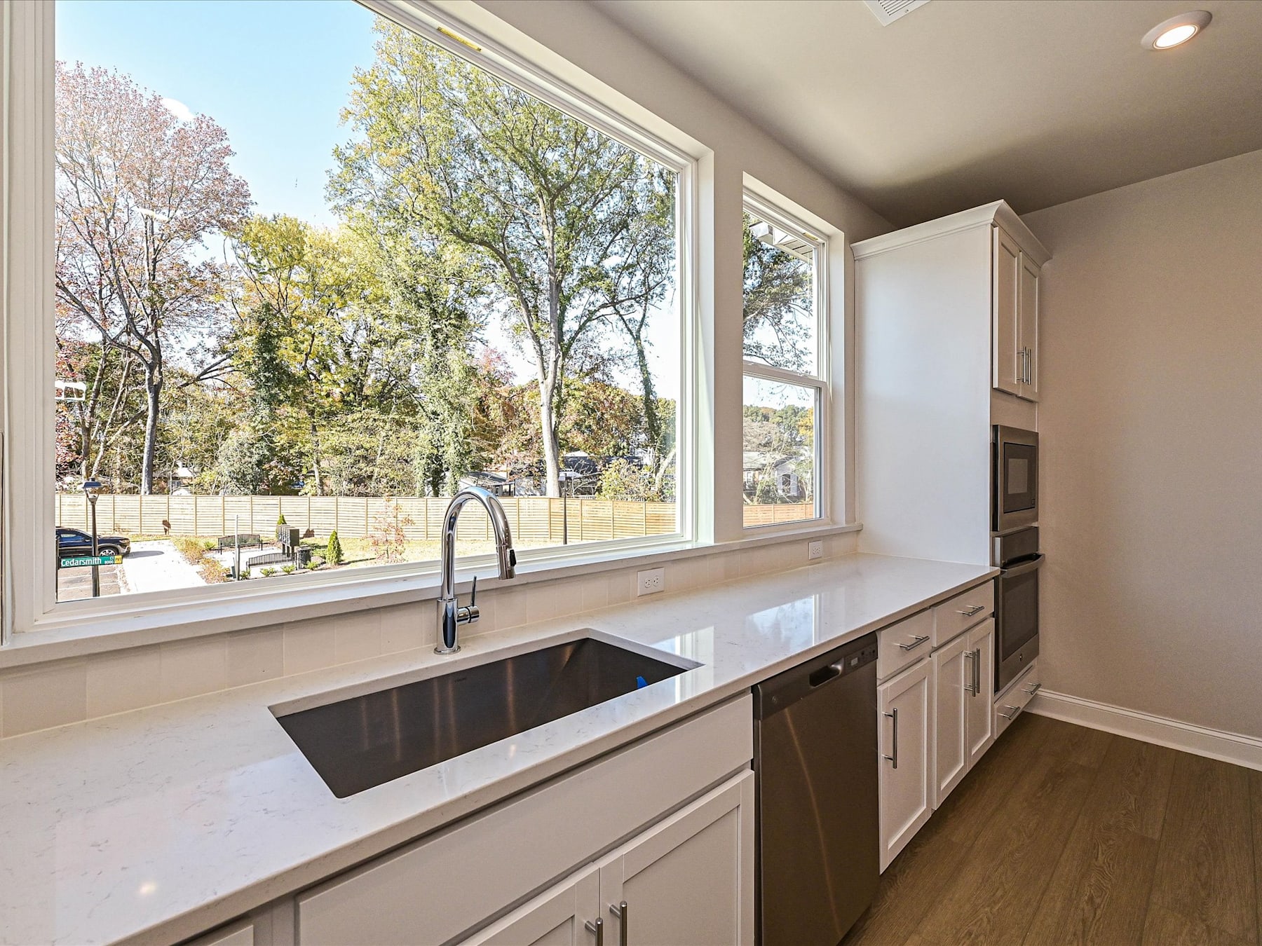 A modern kitchen with a large window overlooking a lush, tree-lined outdoor scene.