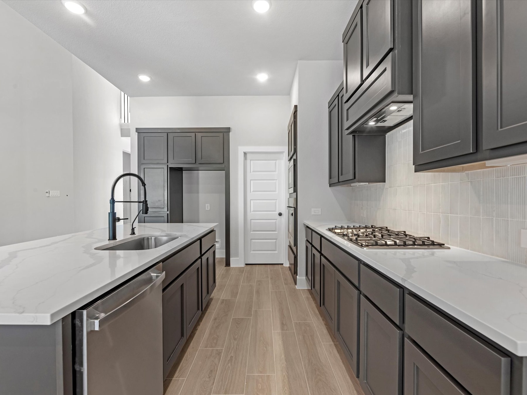 A modern, minimalist kitchen with dark gray cabinets, white countertops, and a sleek stainless steel appliance set against a bright, airy background.