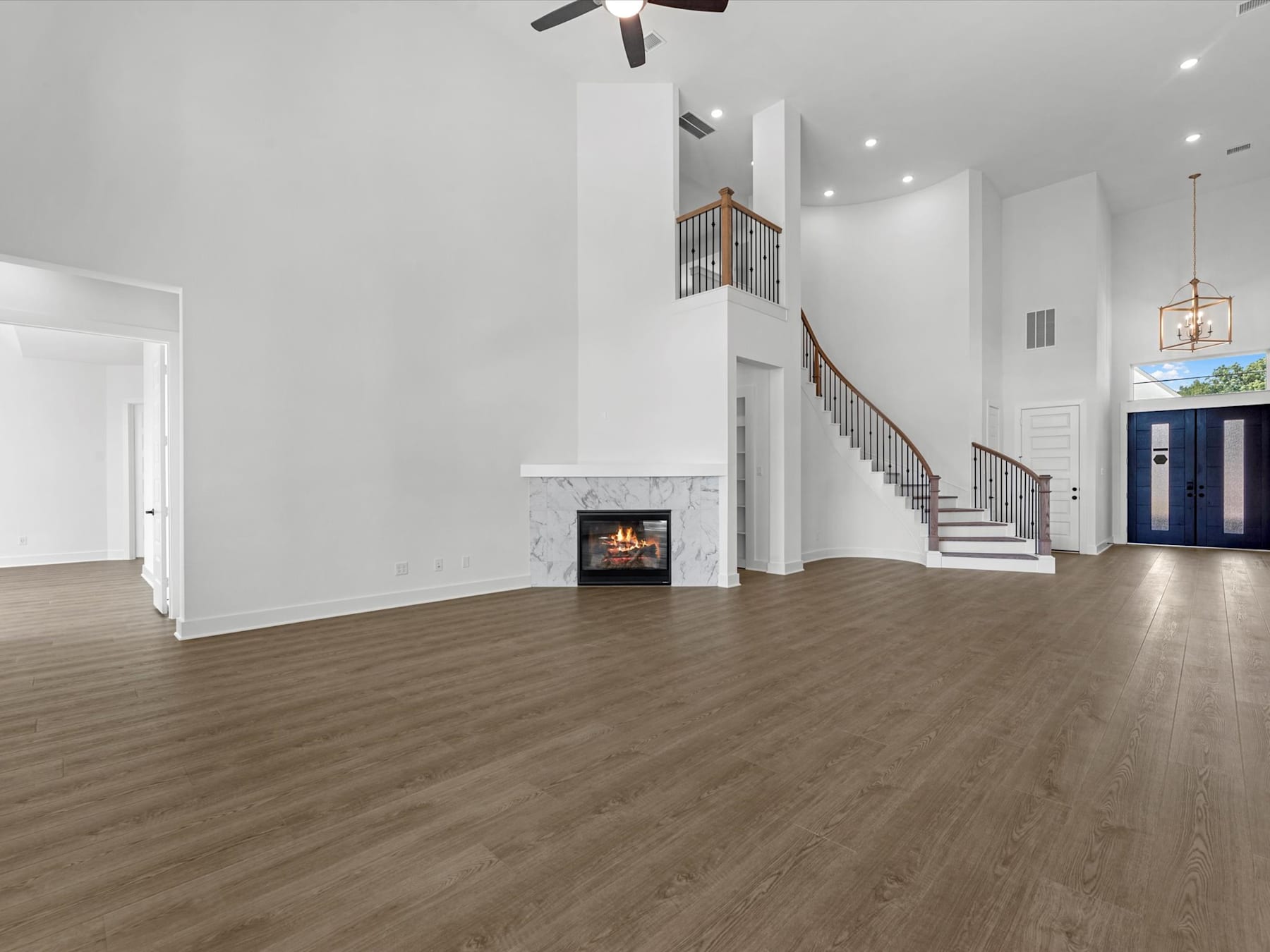 A spacious and well-lit living room with a fireplace, hardwood floors, and a staircase leading to an upper level. The room has a modern and minimalist design, creating a warm and inviting atmosphere.