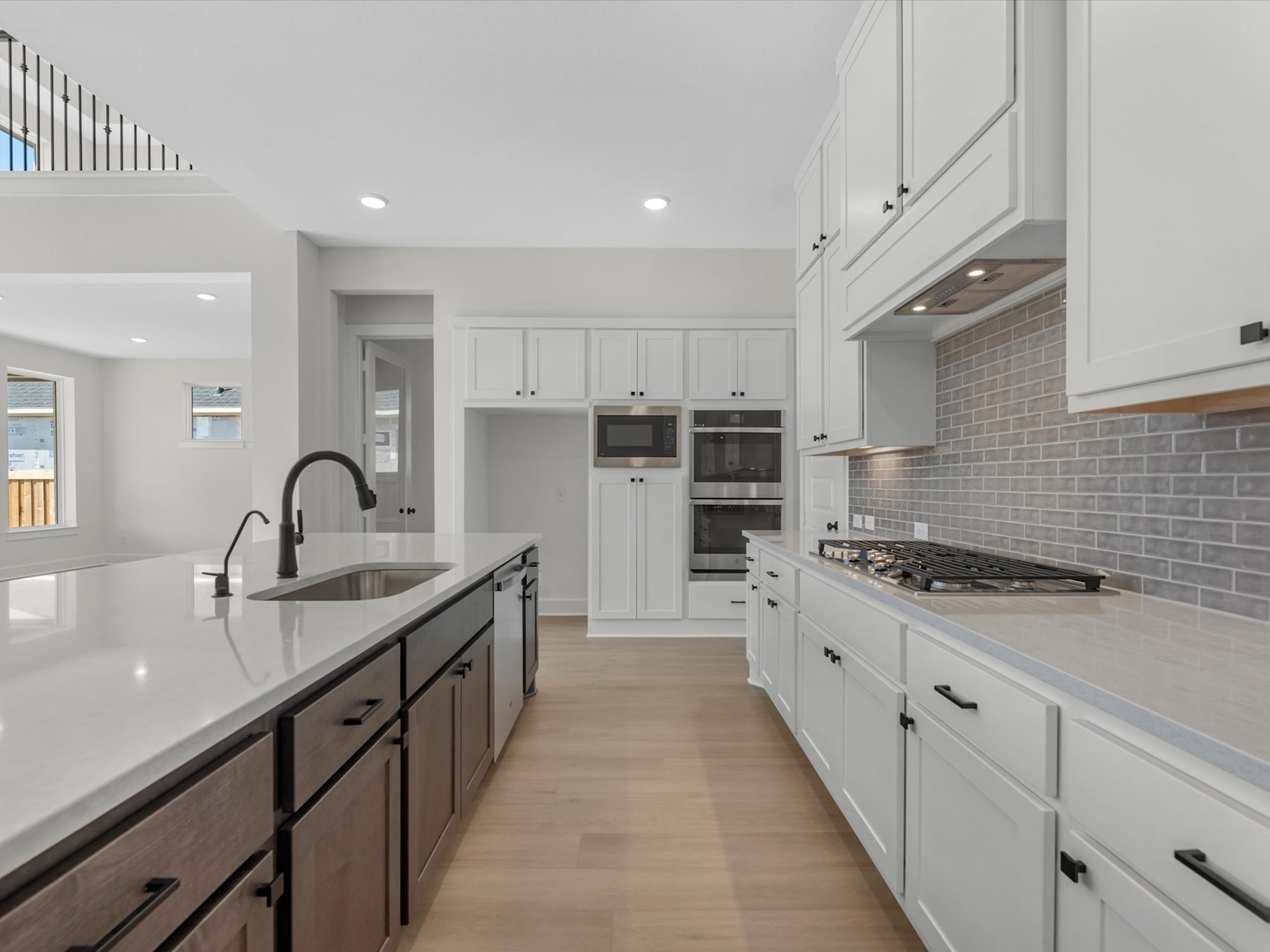 A modern, well-lit kitchen with white cabinets, dark wood drawers, and a tiled backsplash, featuring a central island with a sink and countertop.