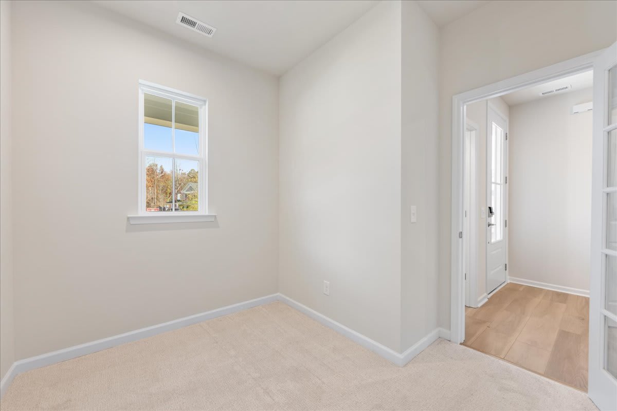 A bright, spacious room with a large window overlooking a scenic outdoor view, featuring hardwood floors and a doorway leading to another area.