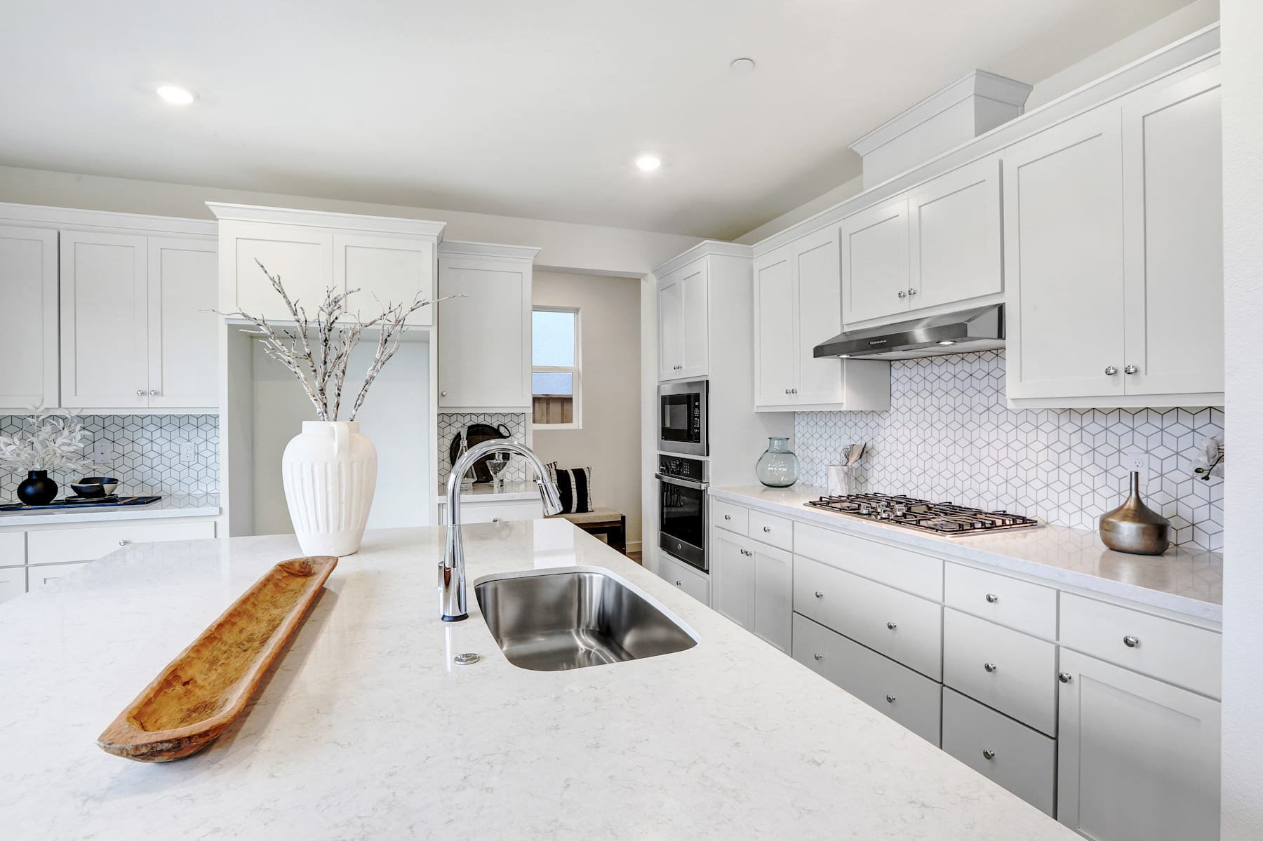 A modern, bright, and spacious kitchen with white cabinets, a stainless steel sink, and a decorative vase on the counter.