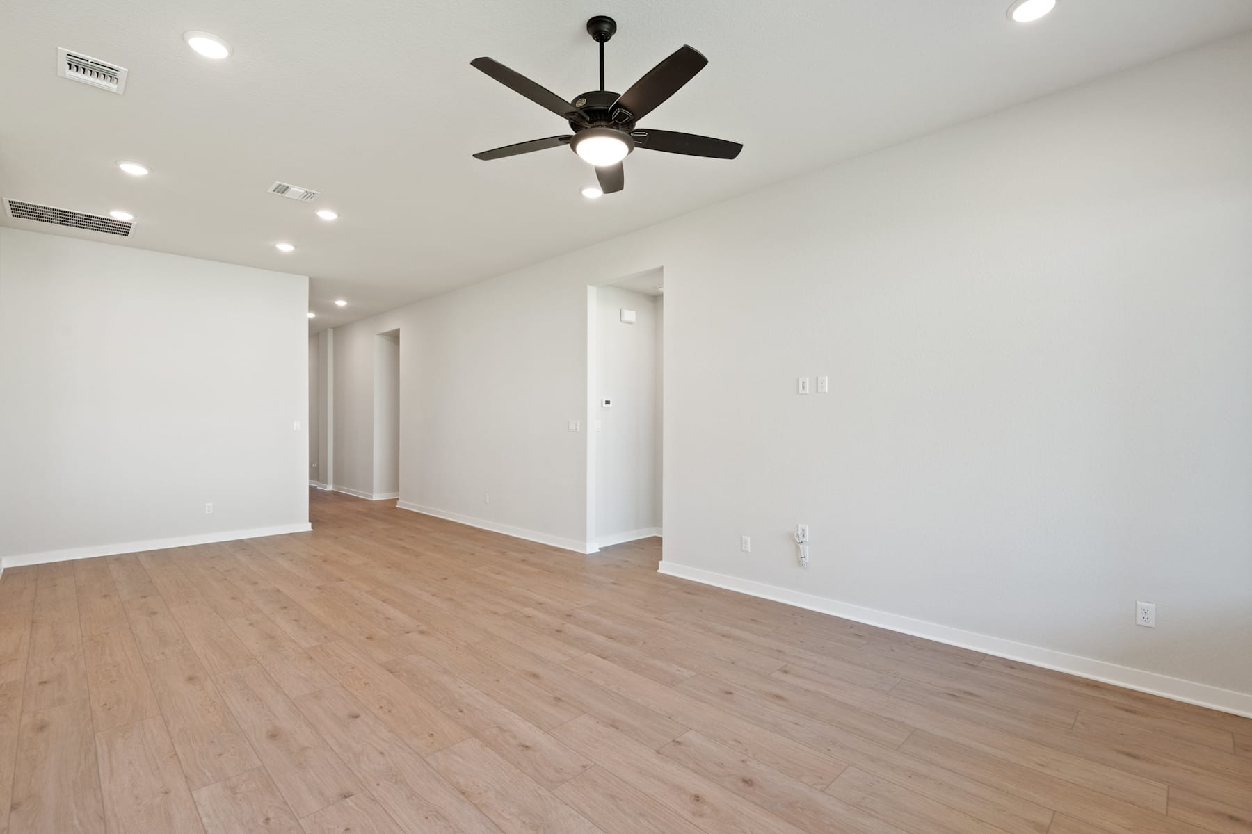 A spacious, well-lit room with a ceiling fan and hardwood flooring, creating a clean and minimalist atmosphere.