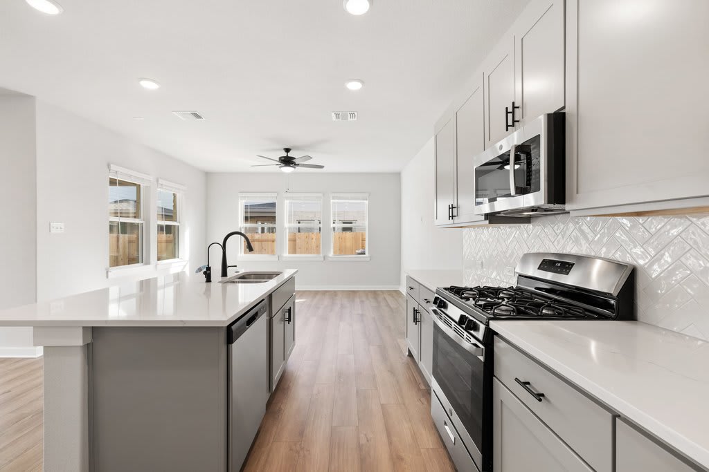 A modern, well-lit kitchen with white cabinets, stainless steel appliances, and a hardwood floor.