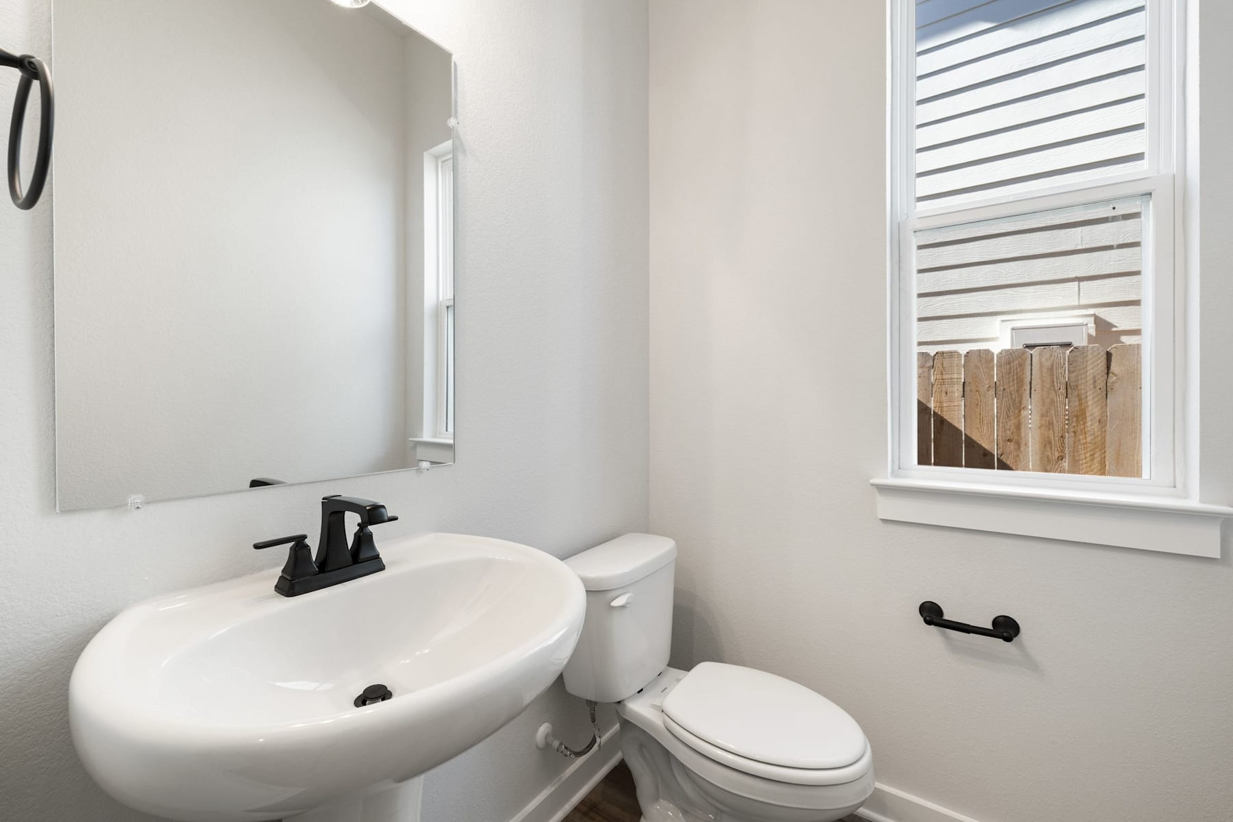 A clean, modern bathroom with a white sink, toilet, and a window overlooking a wooden fence in the background.