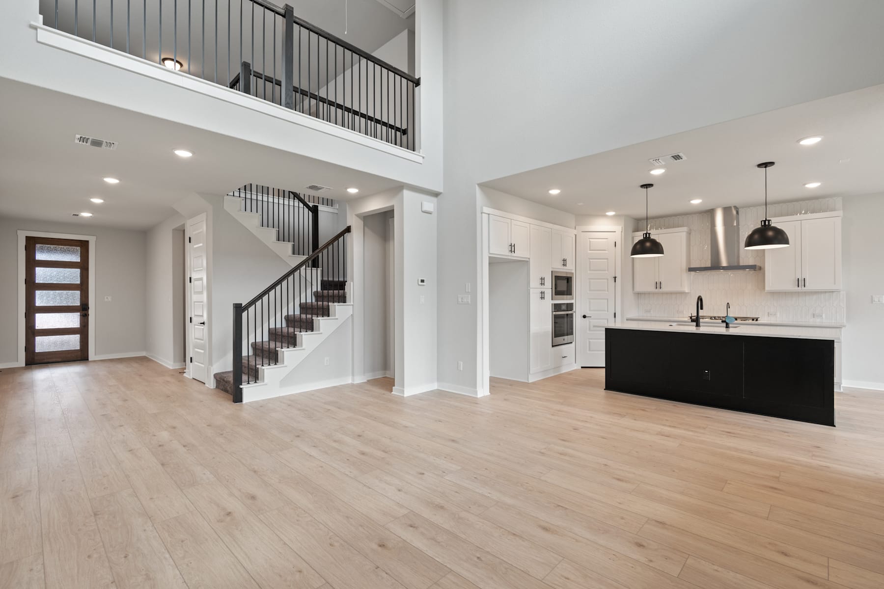 A spacious and modern interior with a staircase, hardwood floors, and a kitchen visible in the background.