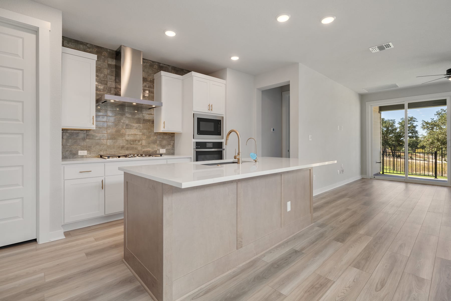 A modern, open-concept kitchen with white cabinets, a large island, and hardwood flooring, set against a backdrop of a bright, airy living space.