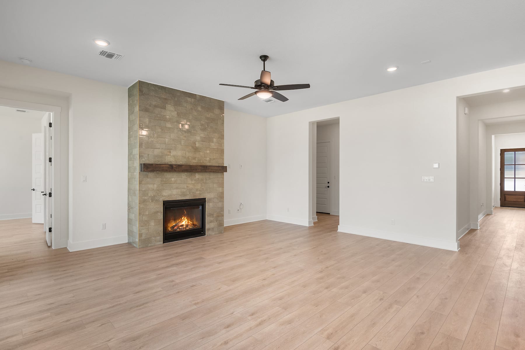 A spacious and modern living room with a fireplace, hardwood floors, and a ceiling fan.