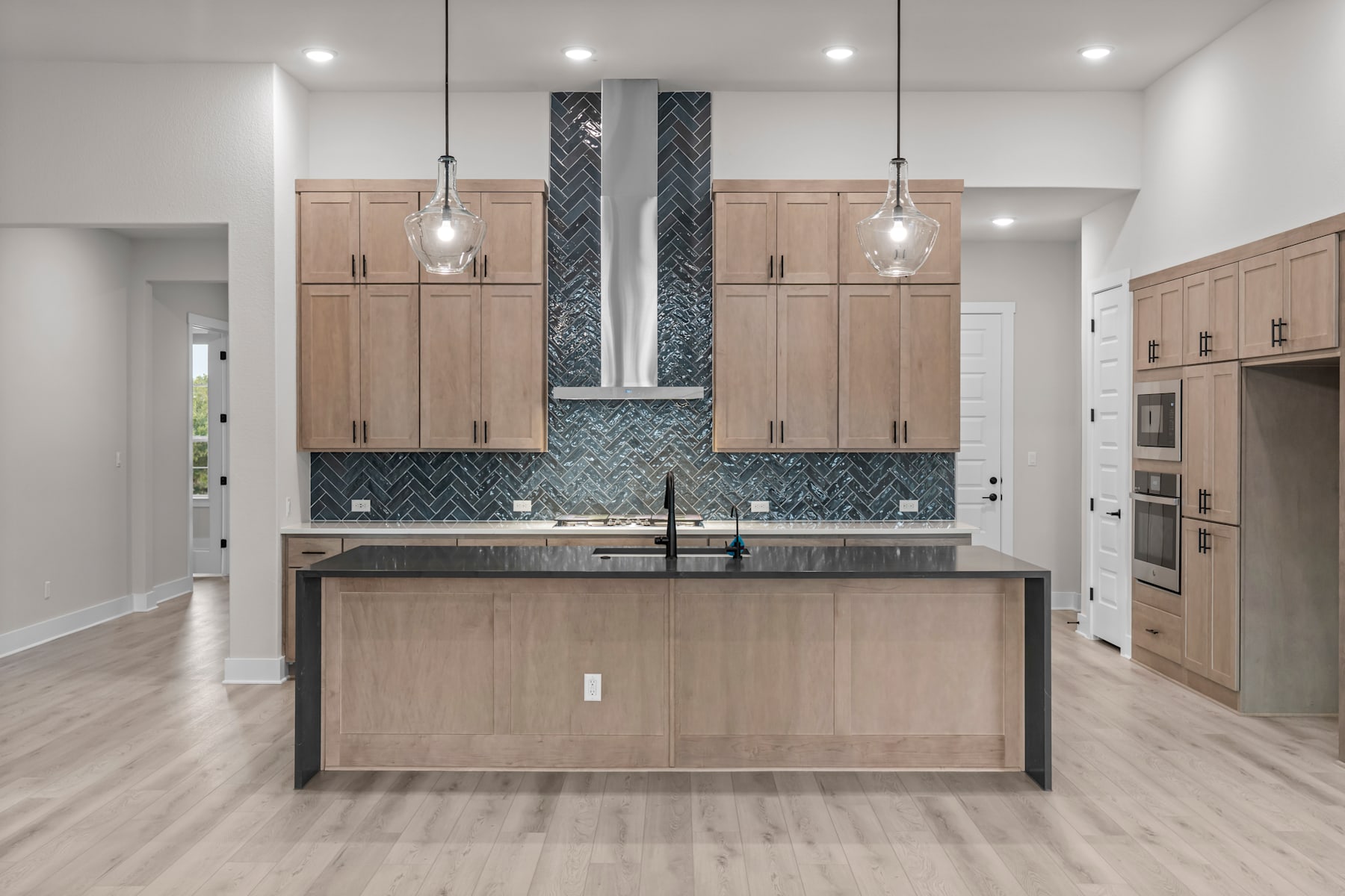 A modern and stylish kitchen with light wood cabinets, a central island, and a patterned tile backsplash, set against a bright and airy background.