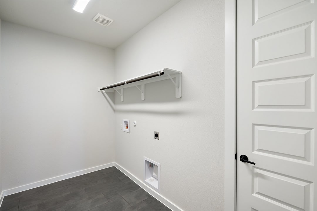 A simple, minimalist room with a white wall, a white door, and a metal shelf or rack mounted on the wall.
