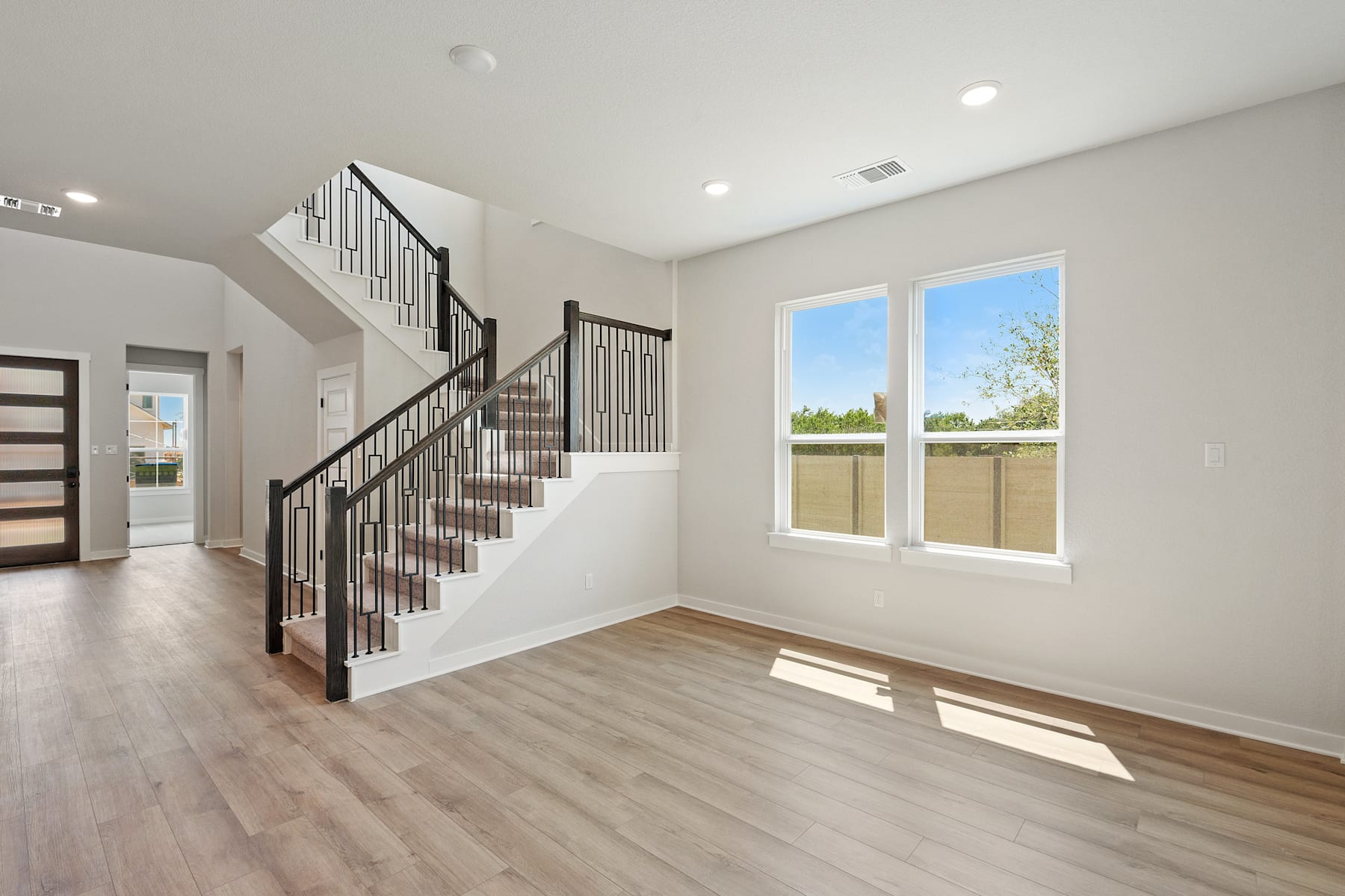 A spacious and bright interior with a wooden staircase, hardwood floors, and large windows overlooking a scenic outdoor view.