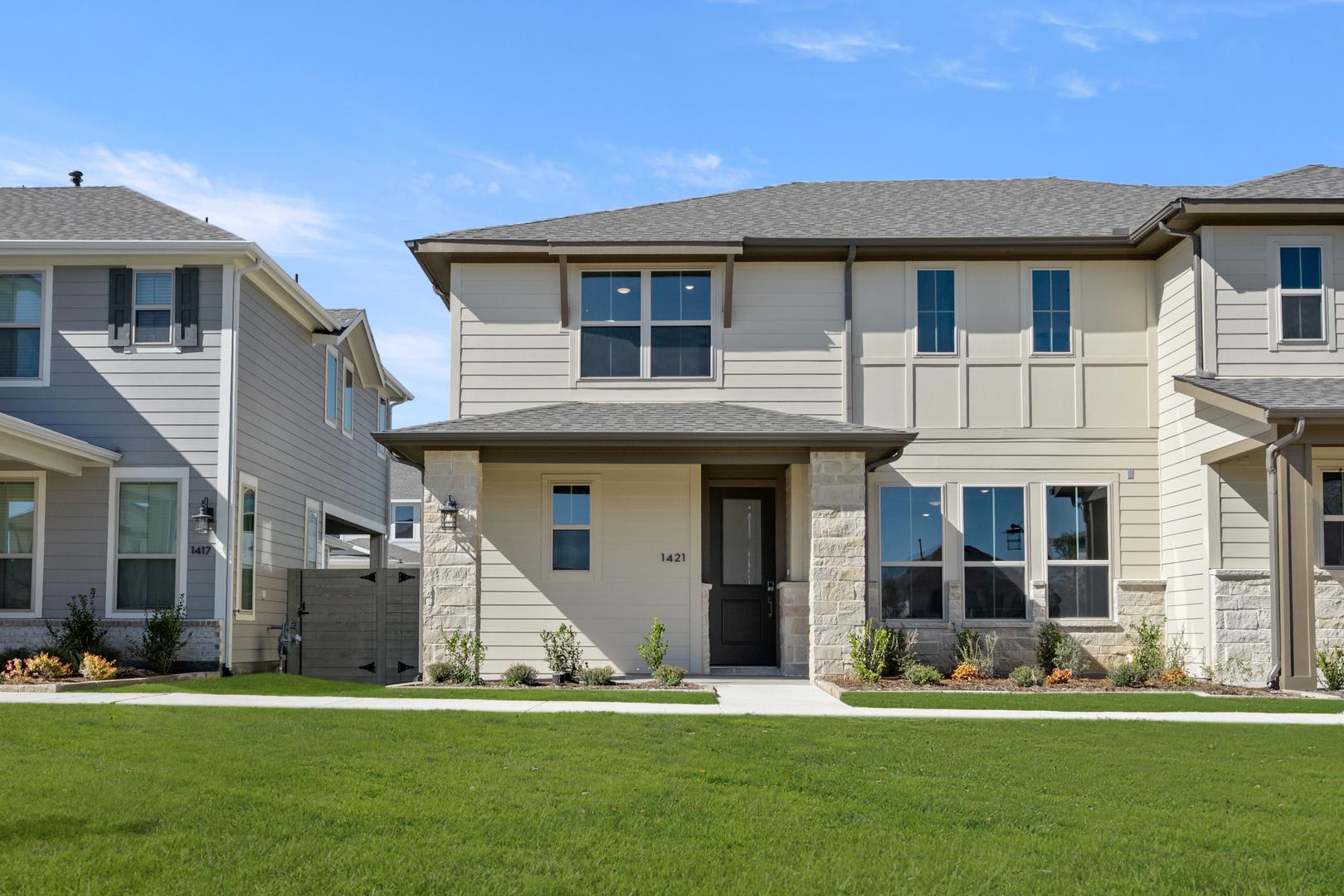 A well-maintained residential neighborhood with a two-story house featuring a neatly landscaped front yard and a paved driveway leading to the entrance.