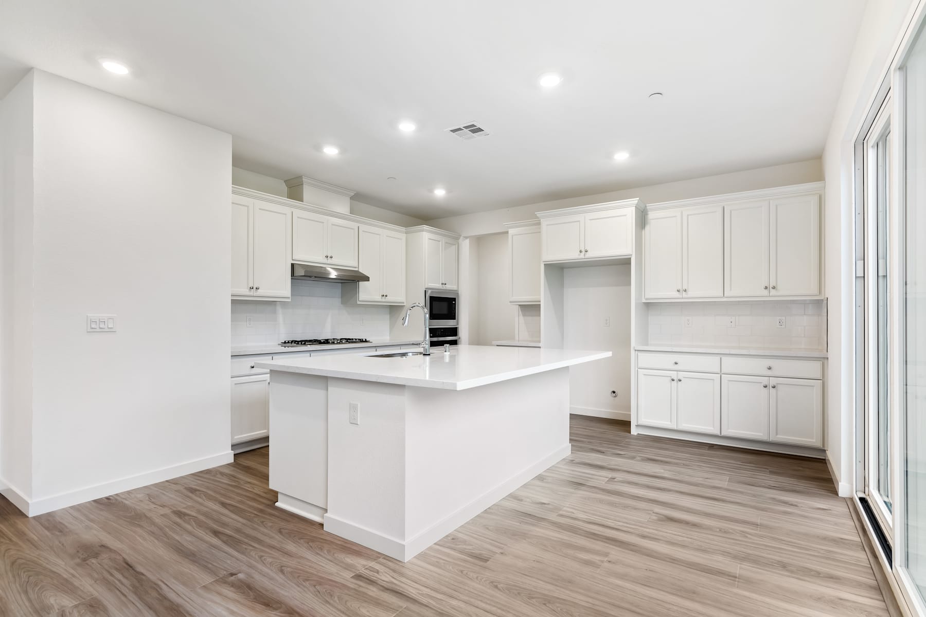 A modern, bright, and spacious kitchen with white cabinets, a central island, and hardwood flooring.