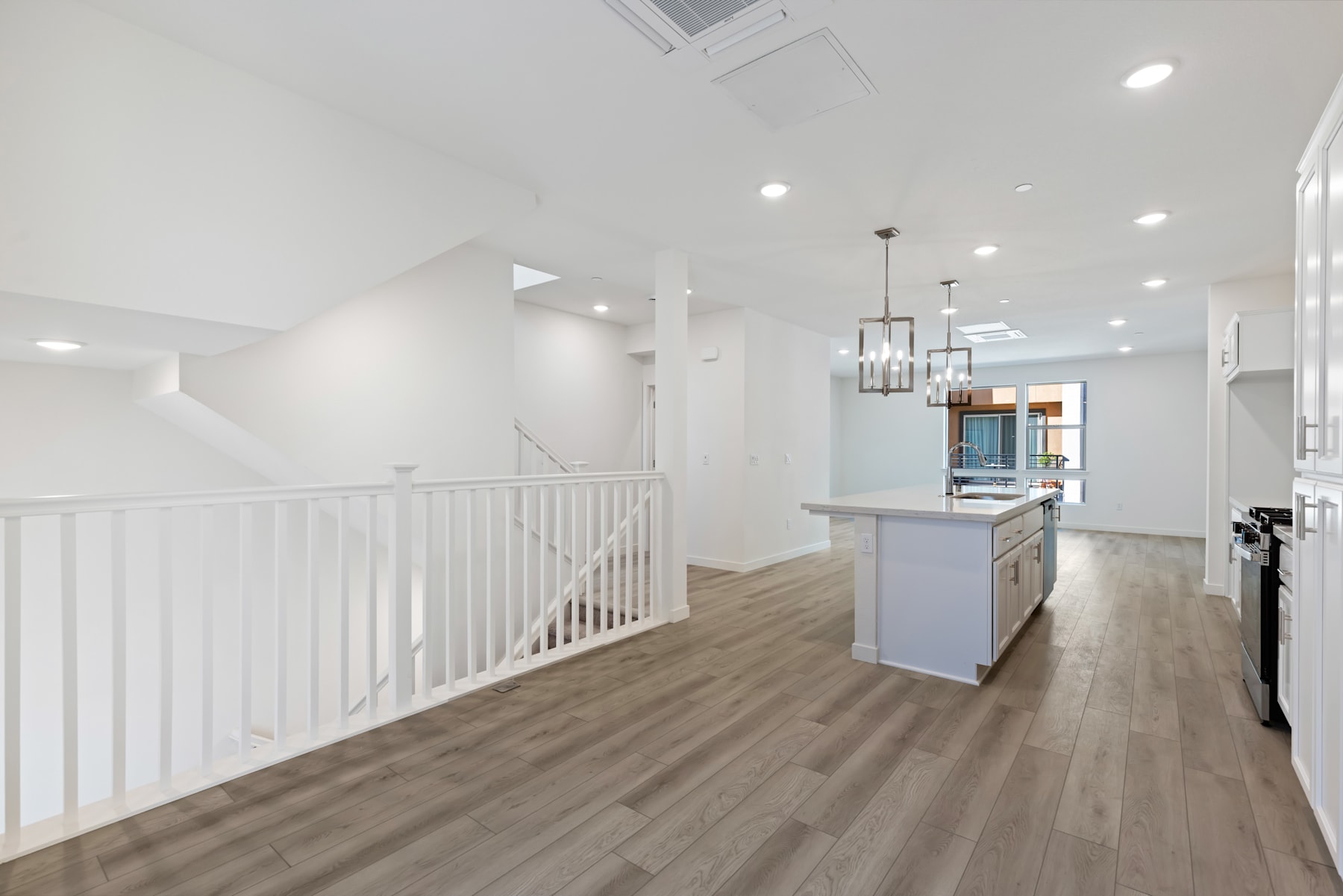 A bright and spacious interior with a wooden floor, a kitchen island, and a staircase with a white railing leading to an upper level.