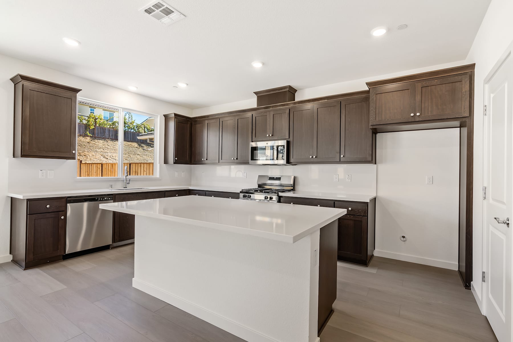 A modern, well-equipped kitchen with dark wood cabinets, a white countertop, and stainless steel appliances, set against a bright and airy background.