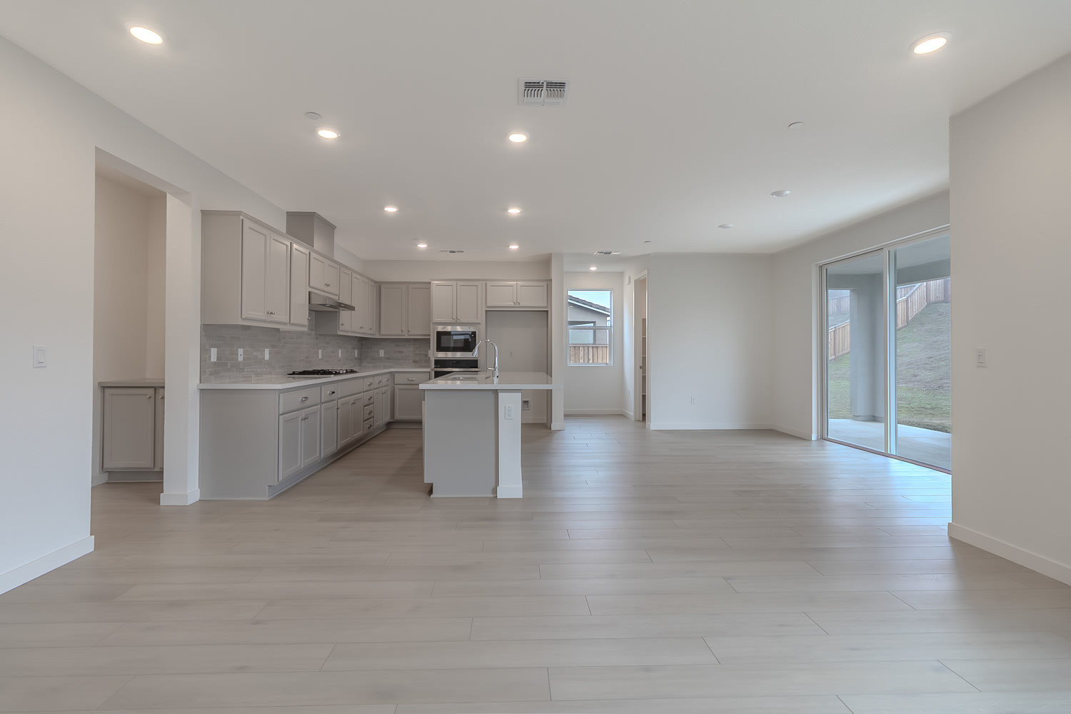 A modern, open-concept kitchen and living space with light-colored cabinets, stainless steel appliances, and a sliding glass door leading to an outdoor area.