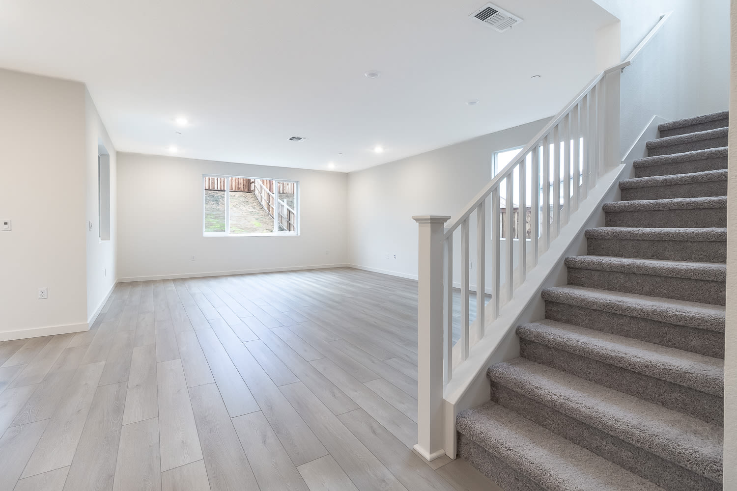 An empty, spacious room with a staircase leading up to the second floor, featuring hardwood floors and a clean, minimalist design.