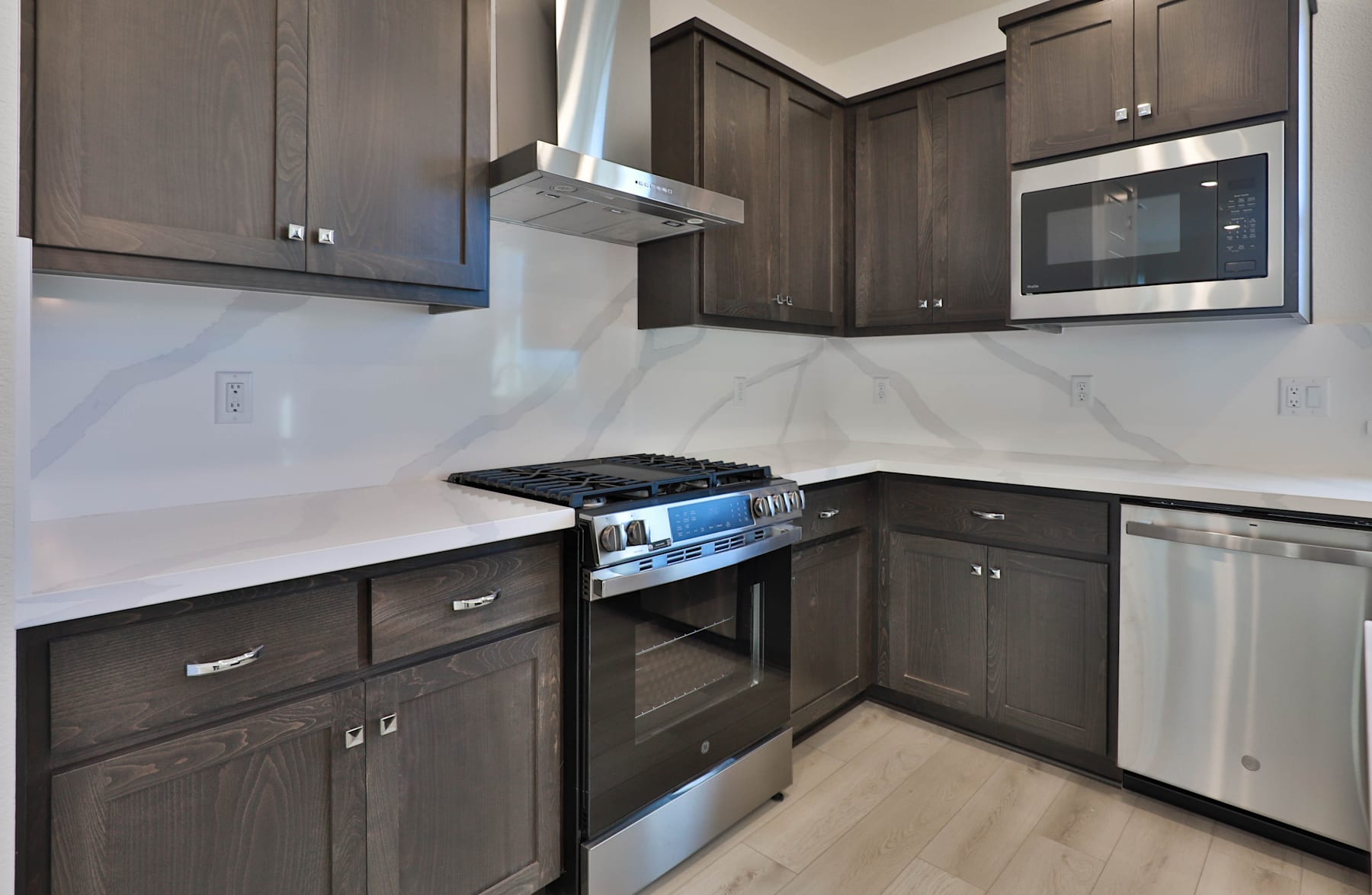A modern kitchen with dark wood cabinets, a white countertop, and stainless steel appliances, including a gas stove and oven.