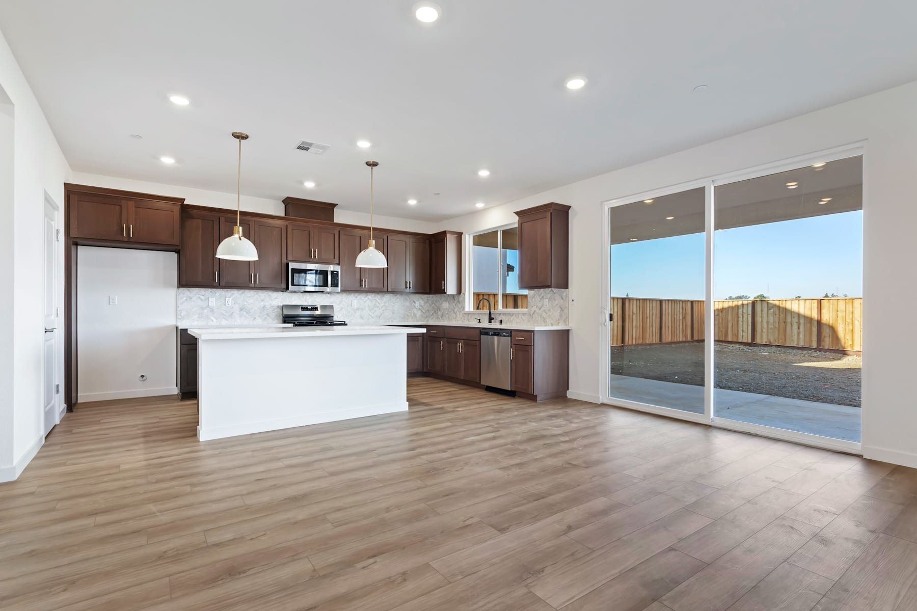 A modern, open-concept kitchen with dark wood cabinets, stainless steel appliances, and a sliding glass door leading to a backyard area.