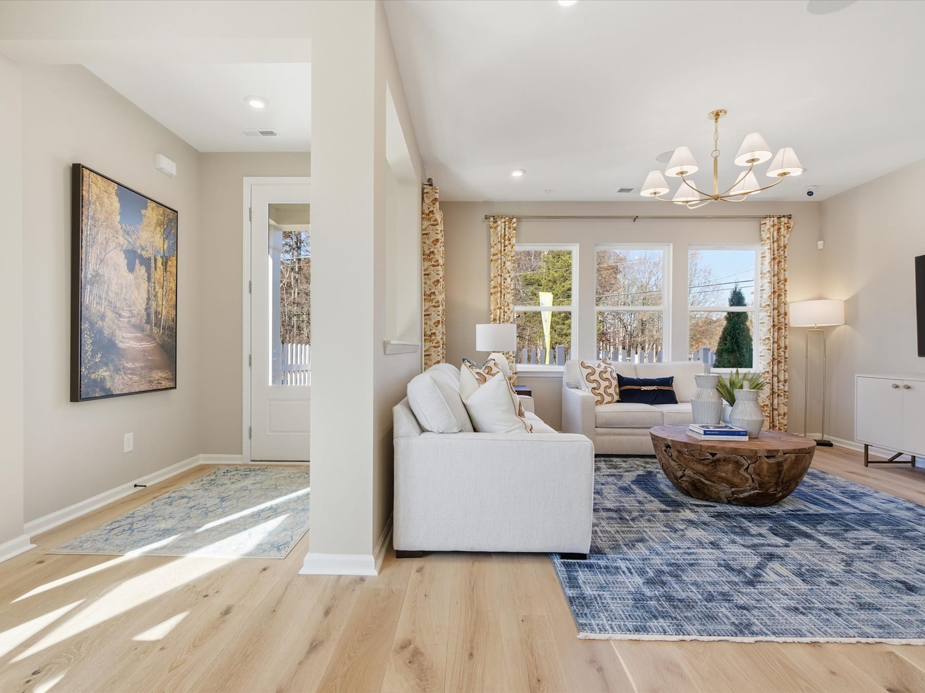 A spacious and well-lit living room with a white sofa, a large area rug, and a decorative artwork on the wall, creating a cozy and inviting atmosphere.