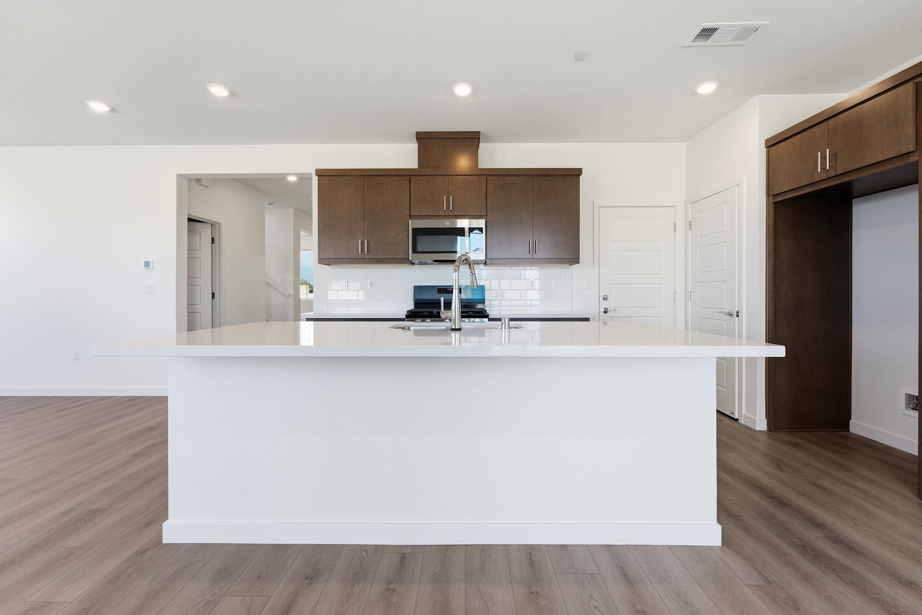 A modern, open-concept kitchen with white walls, dark wood cabinets, and a central island with a white countertop.