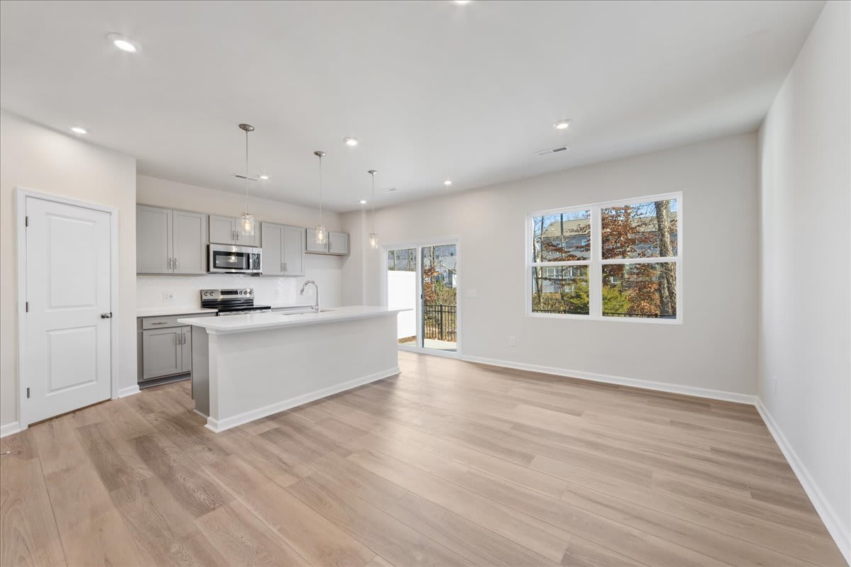 A bright and spacious kitchen with white cabinets, stainless steel appliances, and a large window overlooking a wooded outdoor scene.