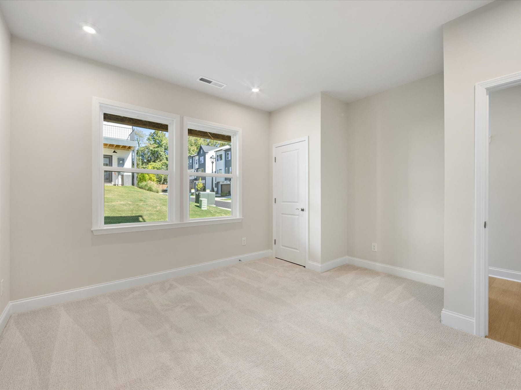 A bright and spacious room with large windows overlooking a lush outdoor area, featuring a clean and minimalist interior design with hardwood floors.