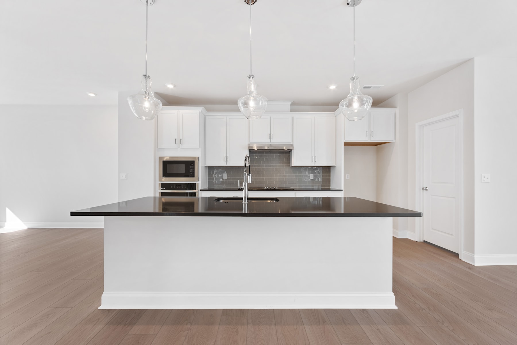A modern, open-concept kitchen with white cabinets, stainless steel appliances, and a dark countertop island in the foreground, set against a bright, airy background.